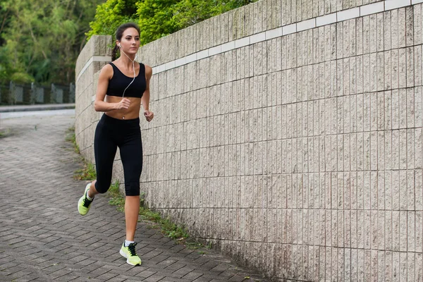 Fit jonge vrouwelijke jogger jogging op de stoep in de buitenwijken. Mooi meisje uit buitenshuis te werken. — Stockfoto