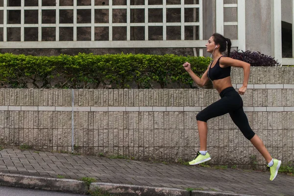 听音乐和慢跑人行道在镇上的年轻女子赛跑运动员的侧视图 — 图库照片