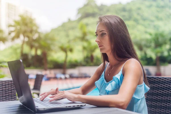 Junge brünette Freiberuflerin in lässiger Kleidung, die im Sommer im Freien an der Laptop-Tastatur arbeitet, verschwommener Hintergrund — Stockfoto