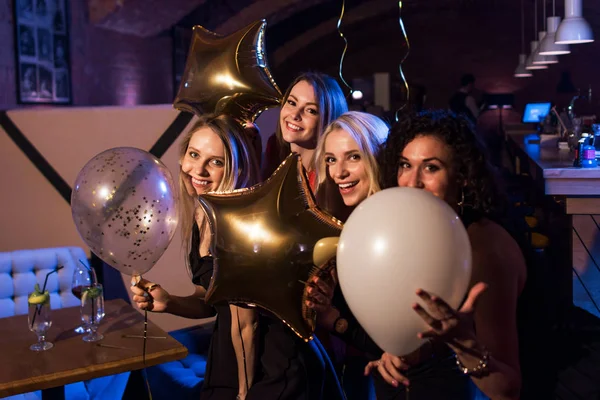 Four beautiful young Caucasian women holding balloons having night out together in trendy bar — Stock Photo, Image