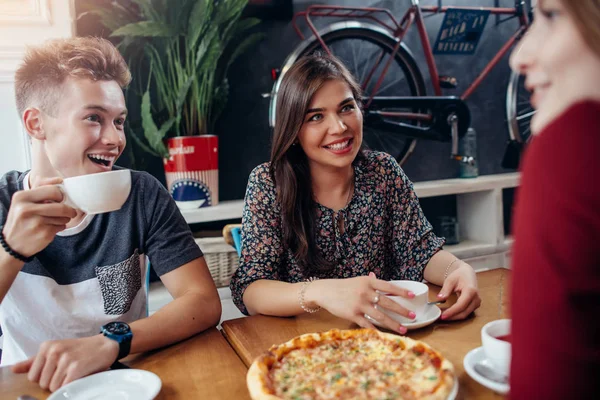 Jóvenes amigos positivos teniendo una pausa para almorzar en la elegante cafetería retro. Chico y chicas pasando un buen rato juntos, hablando, riendo . — Foto de Stock