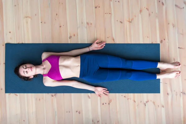 Bovenaanzicht van jonge vrouw liggend in lijk of dode lichaam pose ontspannen na het beoefenen van yoga — Stockfoto