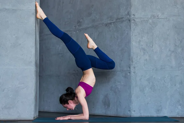 Schlanke Joggerin in Sportbekleidung, die eine Inversion durchführt oder auf dem Kopf stehend auf den Unterarmen balanciert — Stockfoto