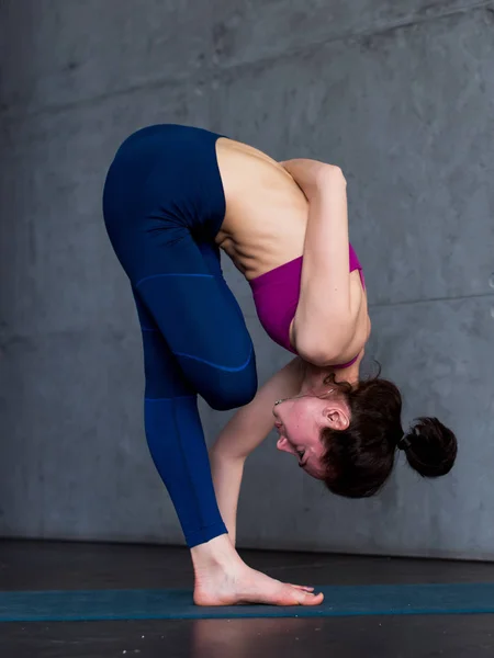 Гибкая молодая женщина, выполняющая упражнения на равновесие на одной ноге, наполовину связанный лотос, стоя впереди, позирует в помещении — стоковое фото