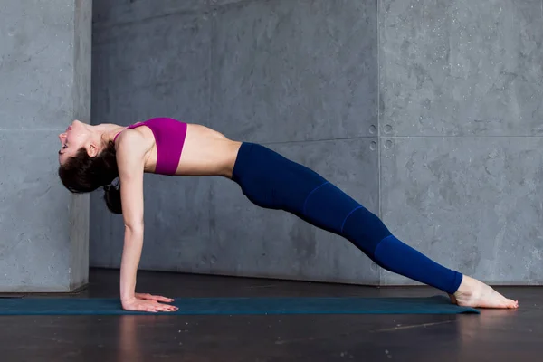Ziemlich dünne Frau in Sport-BH und Leggings, die Yoga nach oben gerichtete Planke Pose, purvottanasana, Training drinnen — Stockfoto
