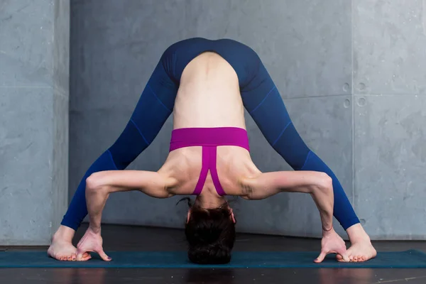 Fullängds framifrån av sportig ung kvinna utövar yoga gör stående grenslar framåt bend pose, Prasarita Padottanasana, projektutkasten inomhus — Stockfoto