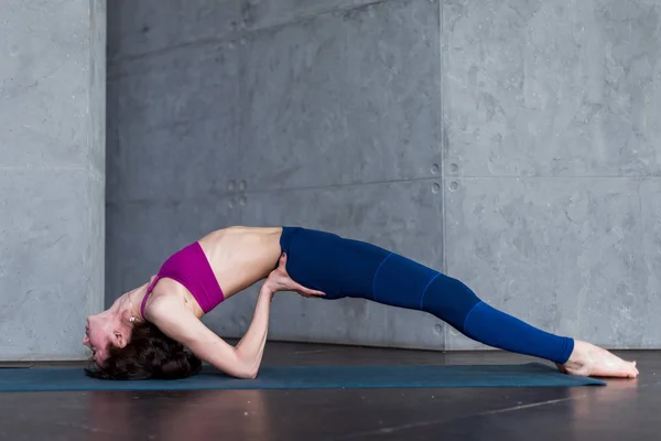 Sidovy av mager ung yogini stående i yoga backbend posera på matta i studio — Stockfoto