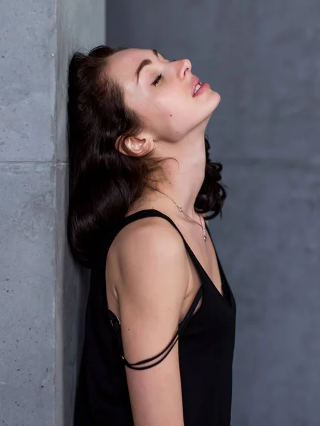 Портрет красивой молодой женщины с каштановыми волосами, стоящей у стены с закрытыми глазами и выражением удовольствия на лице — стоковое фото