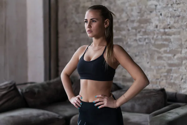 Modelo femenino sexy en ropa deportiva negra con cola de caballo posando en el interior del loft mirando lejos de la cámara — Foto de Stock