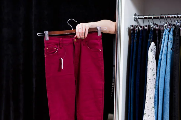 Žena se snaží na kalhoty v obchodě s oděvy natáhl ruku z vybavení pokoje drží kalhoty — Stock fotografie