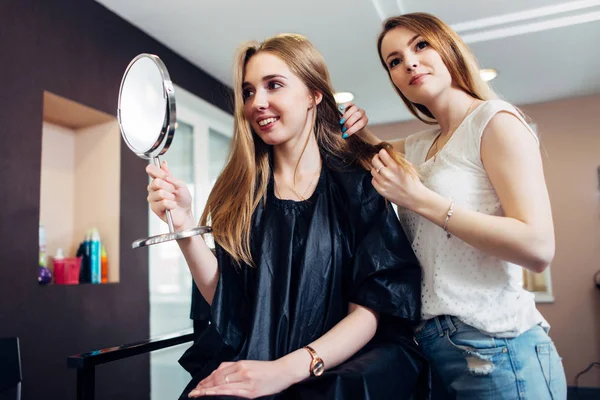 Joven estilista femenina discutiendo y eligiendo un nuevo look para un cliente sentado en la silla mirando en espejo de maquillaje en el salón de belleza —  Fotos de Stock