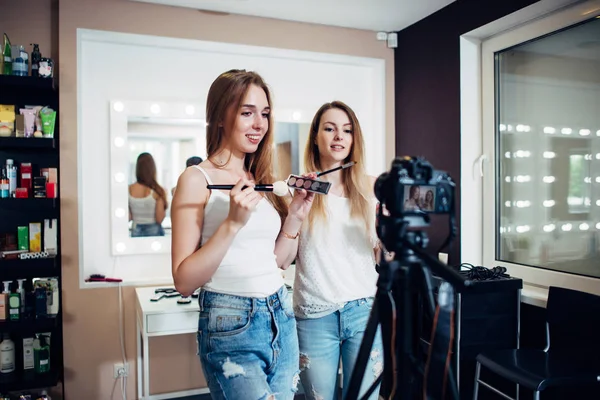 Two friends doing a makeup products review shooting a video blog standing in front of camera — Stock Photo, Image