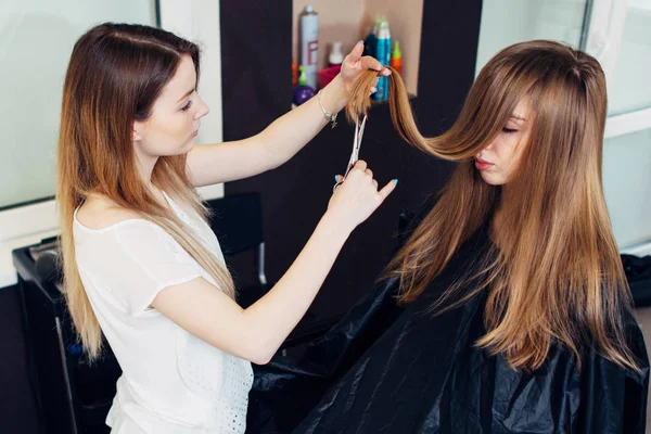 Mladí kosmetička ořezávání či stříhání rozdělit poškozené konce klienta s dlouhými vlasy v salónu krásy — Stock fotografie
