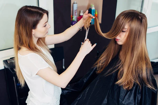 Jonge schoonheidsspecialiste knippen of snijden gespleten beschadigde punten van cliënt s lange haren in de schoonheidssalon — Stockfoto