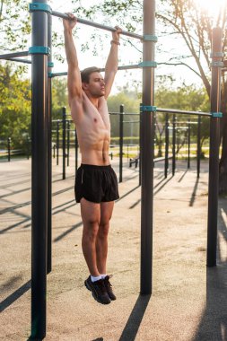 Parkta yatay bir çubuk ile düz silah asılı pull-up egzersizleri yapıyor genç kas atlet.
