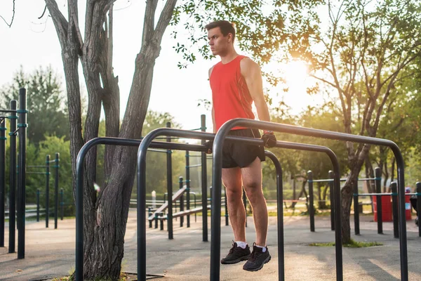 Fit hombre haciendo tríceps inmersiones en barras paralelas en el parque haciendo ejercicio al aire libre —  Fotos de Stock