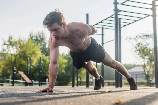 Sportler junger Mann beim einarmigen Liegestütz, der im Sommer draußen seine Oberkörpermuskulatur trainiert. — Stockfoto