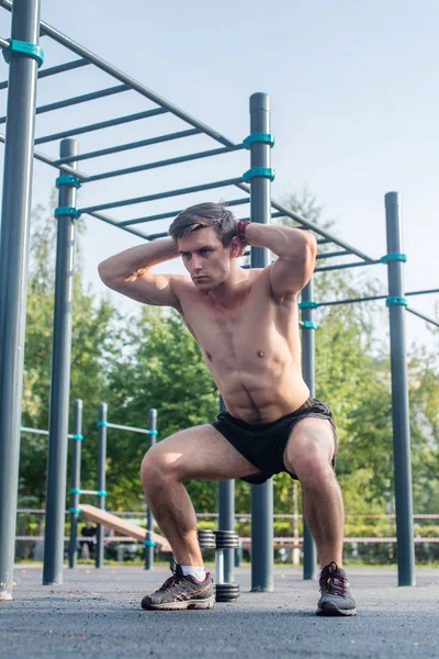 Muskulöser Fitness-Athlet macht Kniebeugen mit den Händen hinter dem Kopf und trainiert im Park. — Stockfoto