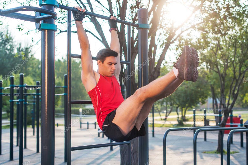 Fitnes man hanging on wall bars performing legs raises. Core cross training working out abs muscles