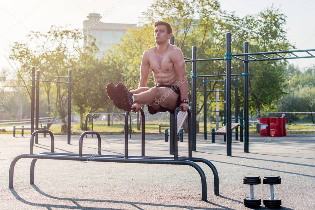 Young strong athlete working out in outdoor gym, doing leg lifting abs exercise.