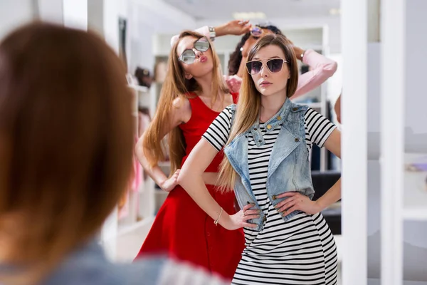 Meninas glamourosas experimentando óculos de sol posando na frente do espelho na boutique de moda — Fotografia de Stock