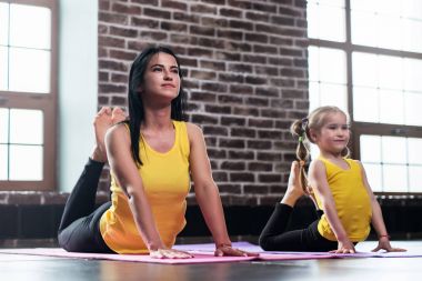 Young mother and her daughter wearing the same sportswear doing king cobra pose during group yoga training clipart