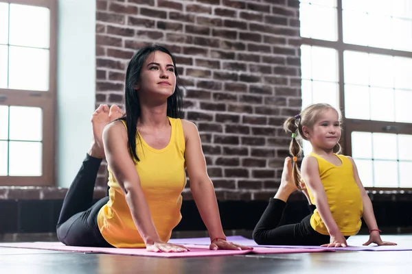 Молода мати та її дочка носять той же спортивний одяг, що робить позу короля кобри під час тренування групової йоги — стокове фото