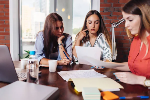 Equipe de trois collègues féminines sérieuses qui cherchent, lisent, étudient les documents qui travaillent au bureau — Photo