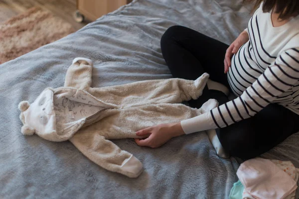 Mulher grávida sonhando e segurando roupas de bebês — Fotografia de Stock