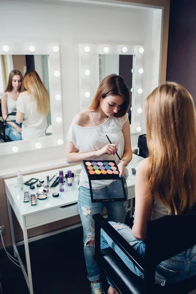 Joven profesional visagiste celebración paleta aplicación de sombra de ojos a la modelo femenina caucásica en salón de belleza — Foto de Stock