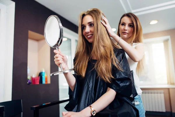 Joven peluquero profesional terminó el corte de pelo y mostrar el resultado al cliente mirando en el espejo sentado en el salón de belleza — Foto de Stock