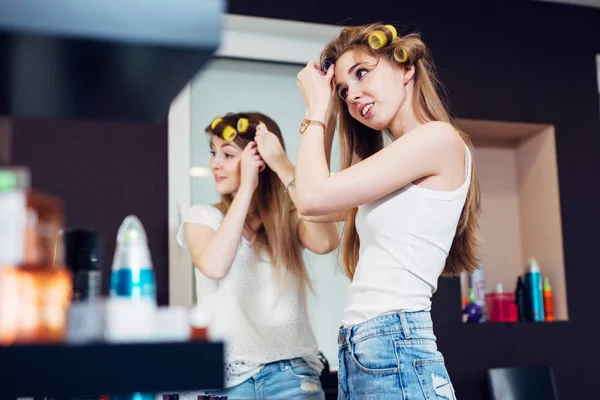 Adolescente niñas aplicando rodillos de pelo en su largo cabello rubio preparándose para salir —  Fotos de Stock