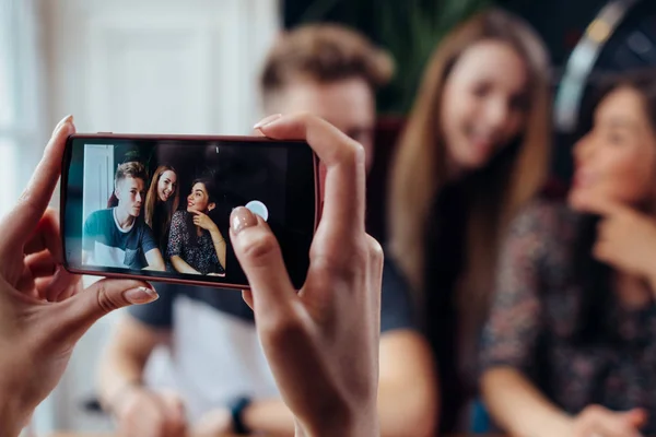 Mãos femininas tirando foto com smartphone de jovens amigos alegres, fundo embaçado — Fotografia de Stock