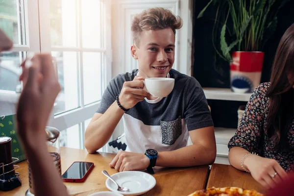 Портрет стильного молодого парня с чашкой чая, завтракающего с друзьями в кафе — стоковое фото