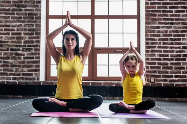 Инструктор по йоге для женщин тренирует маленькую девочку делать упражнения на растяжку сидя в позе лотоса в помещении — стоковое фото