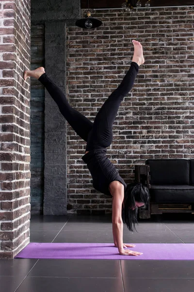 A piedi nudi giovane atleta donna in abiti sportivi neri facendo stand a parete in studio loft . — Foto Stock