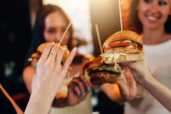 Mãos femininas segurando grandes hambúrgueres suculentos saborosos com mulheres desfocadas no fundo — Fotografia de Stock