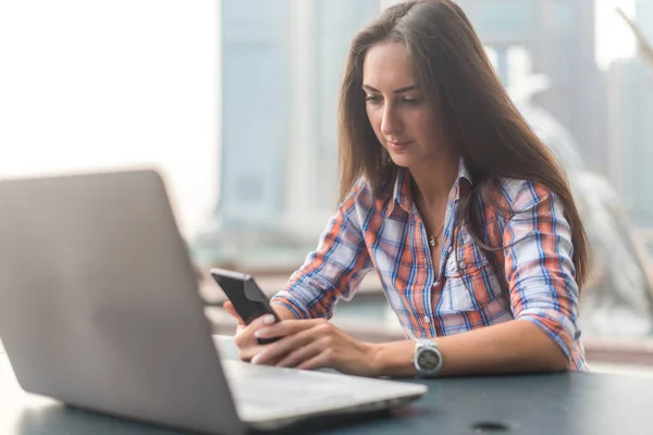 Attraktive junge Frau, die eine SMS auf ihrem Handy liest. Mädchen sitzt mit Smartphone im Freien — Stockfoto