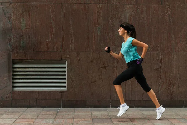 Seitenansicht einer sportlichen jungen Frau, die auf dem Gehweg läuft. — Stockfoto