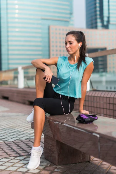 Junge Fitness-Frau ruht sich nach dem Training aus, sitzt auf der Bank in der Innenstadt. — Stockfoto