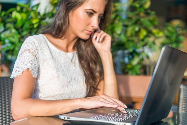 Vista lateral da jovem freelancer ocupada pensando sobre o projeto e trabalhando em seu laptop no café da calçada — Fotografia de Stock