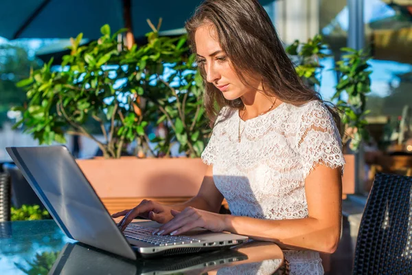 Blogger bastante sonriente usando computadora portátil para escribir blogs mientras está sentado en la cafetería al aire libre en un día soleado . —  Fotos de Stock