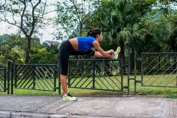 Νέα αθλητική γυναίκα κάνει ασκήσεις προθέρμανσης, τεντώνοντας τα πόδια της σε φράχτη στο δρόμο πριν από την εκτέλεση — Φωτογραφία Αρχείου