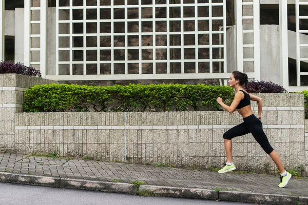 Side view of young female runner listening to music and jogging on sidewalk in town — Stock Photo, Image