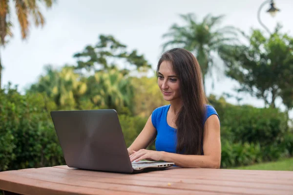 Junge hübsche lächelnde Studentin plaudert mit Freunden auf Laptop im Sommerpark. — Stockfoto