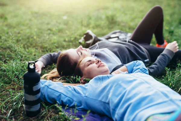 Две юные спортсменки, лежащие на траве с закрытыми глазами, расслабляются после тренировки на открытом воздухе — стоковое фото