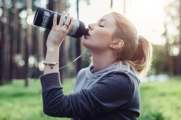 Retrato de la joven deportista en forma con pelo claro bebiendo agua después de los ejercicios de la mañana en el parque — Foto de Stock