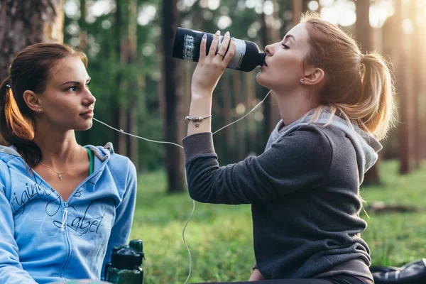 Two female athletes talking a break after training drinking water sitting on ground in the park — Stock Photo, Image