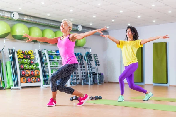 Dois modelos de fitness feminino feliz dançando Zumba, fazendo exercícios aeróbicos trabalhando para perder peso no ginásio com equipamentos coloridos em segundo plano — Fotografia de Stock