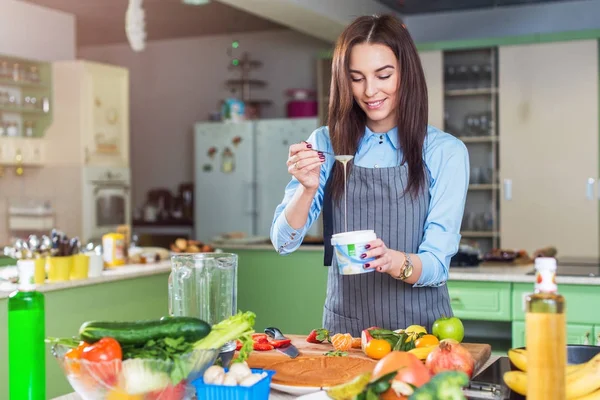 Cheerful young female chef cooking dessert adding condensed milk in dish in her kitchen — Stock Photo, Image